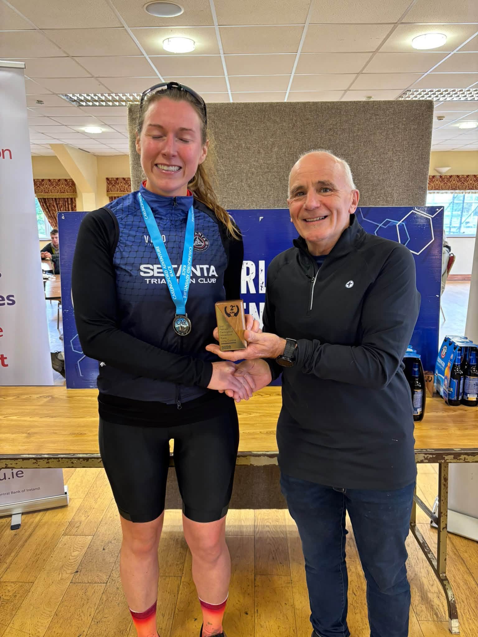 Prize giving: a winner in a Setanta Triathlon Club top, wearing her finisher's medal, is presented with a trophy
