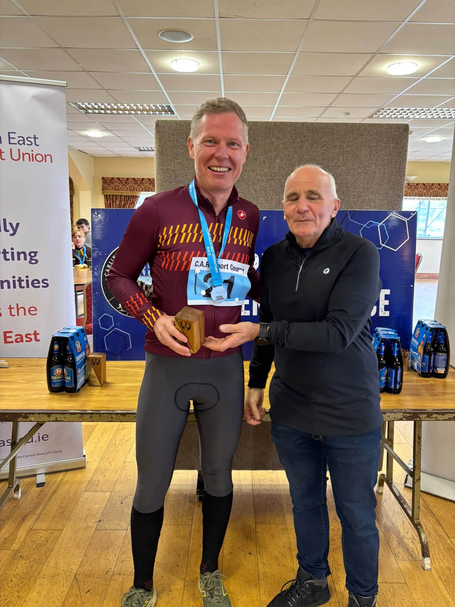 Prize giving: a winner in a maroon cycling jersey and race number is presented with a trophy